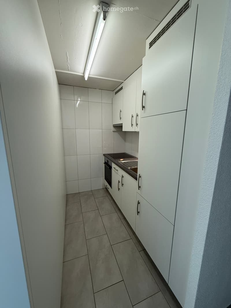 Modern kitchen with white cabinets, tiled walls, and a built-in oven. The space is clean and well-lit with a sleek design.