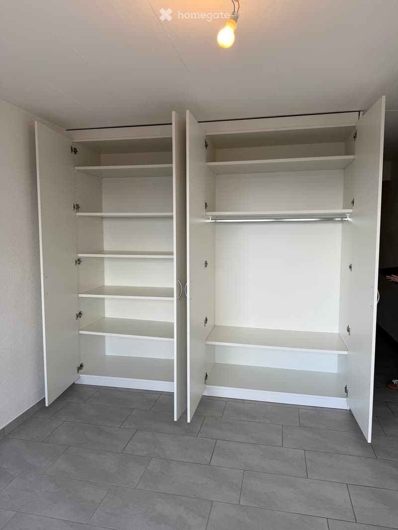 Empty room with white built-in cabinets and shelves, grey tiled floor, and a hanging light fixture.