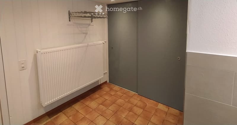 Empty hallway with wooden flooring, white radiator, metal shelf, and grey door.