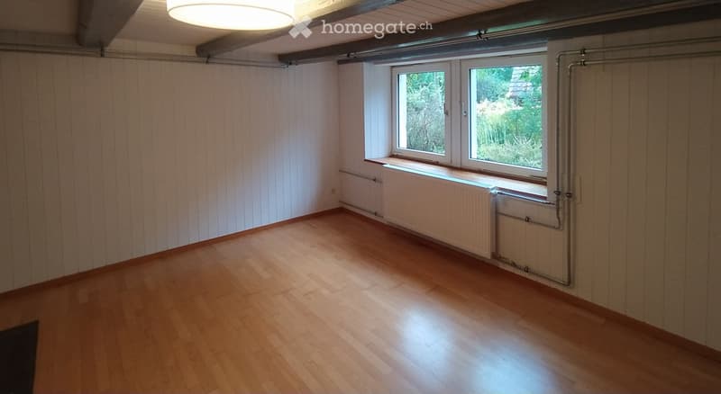 Empty room with wooden flooring, white paneled walls, and large windows with radiators underneath. No furniture or personal items present.
