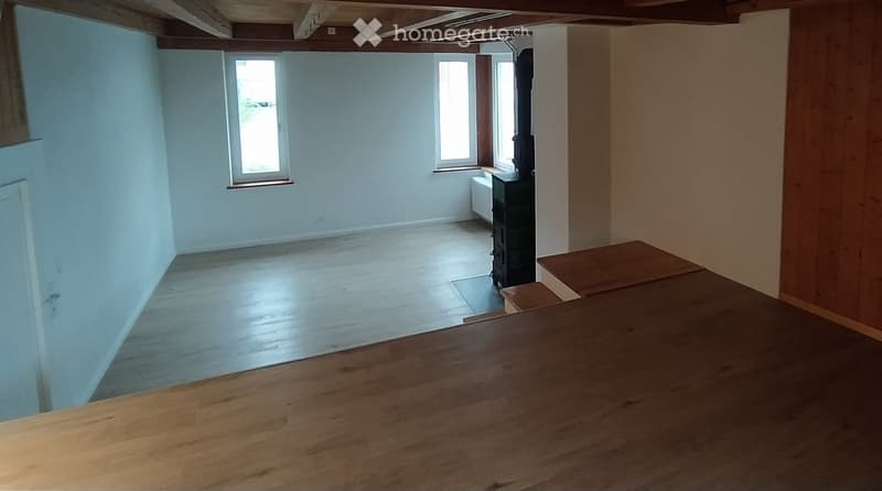 Empty room with wooden flooring, white walls, and three windows. Exposed wooden beams on the ceiling.