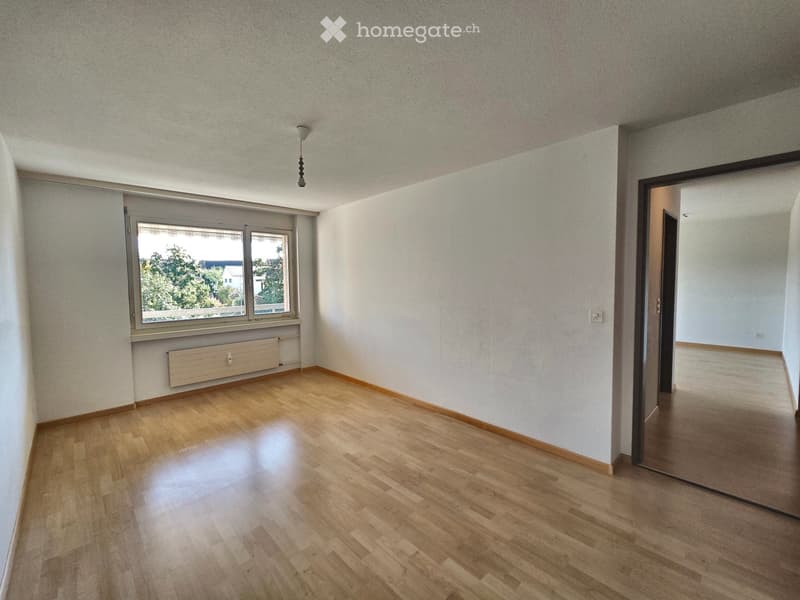 Empty room with wooden flooring, white walls, and a window with a view of greenery. No furniture or equipment is present.