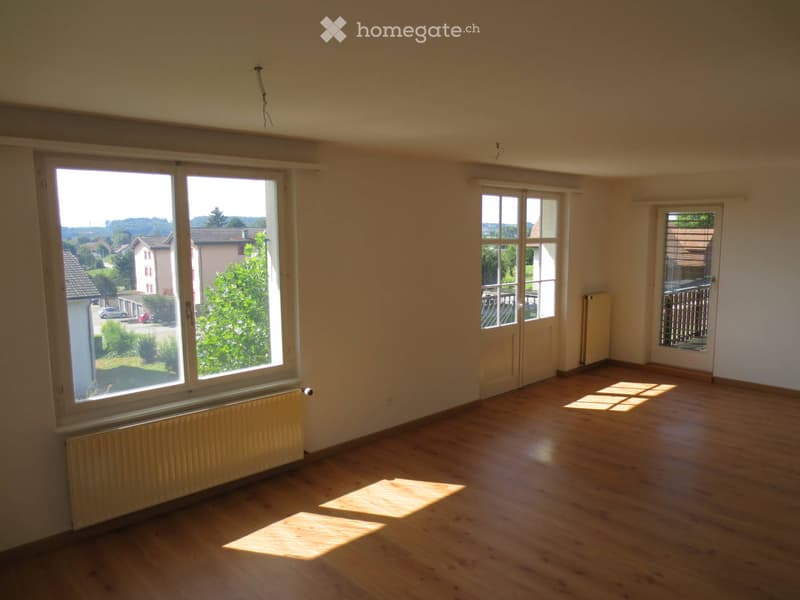 Empty room with wooden flooring, large windows, and radiators. No furniture or equipment present.