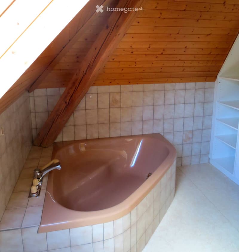 Bathroom with a pink bathtub, tiled walls, wooden ceiling, and a white shelf on the right side.