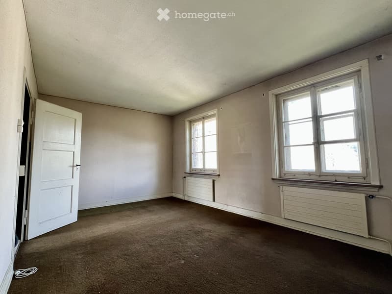 Empty room with beige walls, carpeted floor, two windows with white frames, and a white door leading to another space.