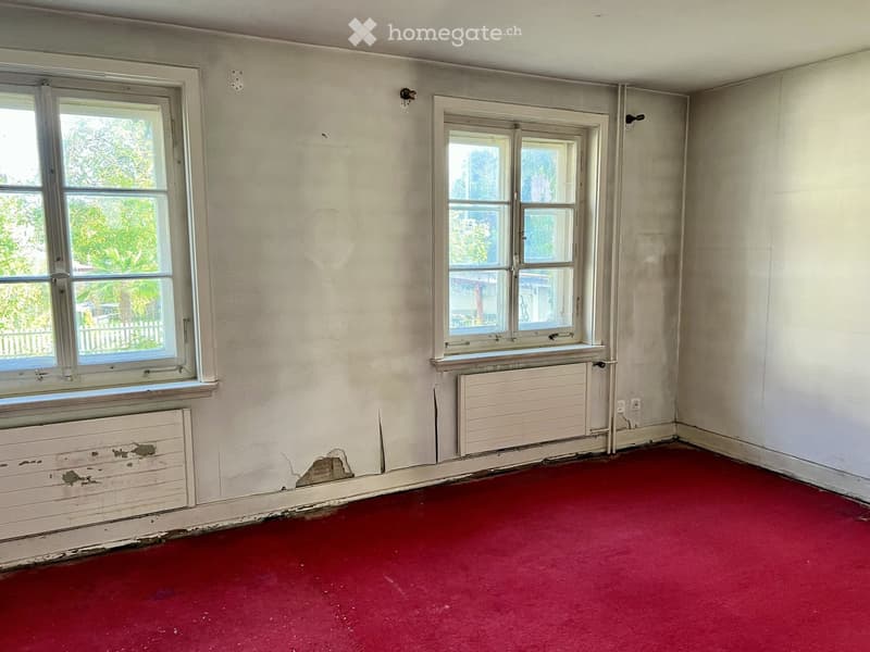 Empty room with red carpet, white walls, two windows, and radiators below them.