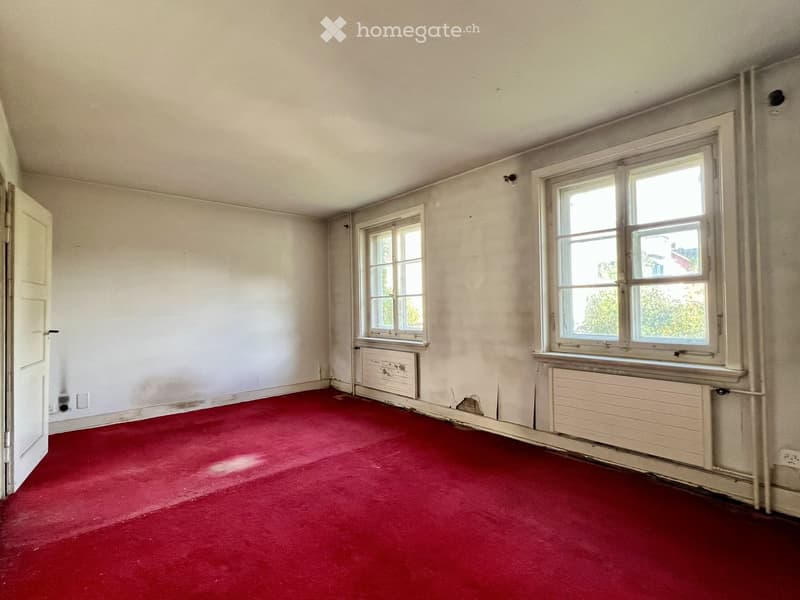 Empty room with red carpeting, white walls, two windows, and a door. No furniture or equipment present.
