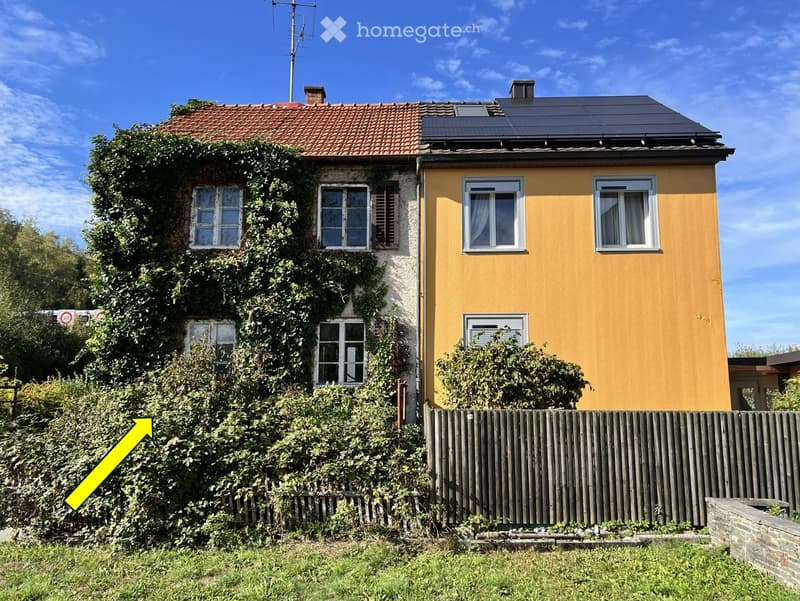 Two-story house with yellow siding, red-tiled roof, and solar panels on the roof. The left side has a brick wall covered in ivy, while the right side is painted yellow with white-framed windows. A wooden fence surrounds the property.