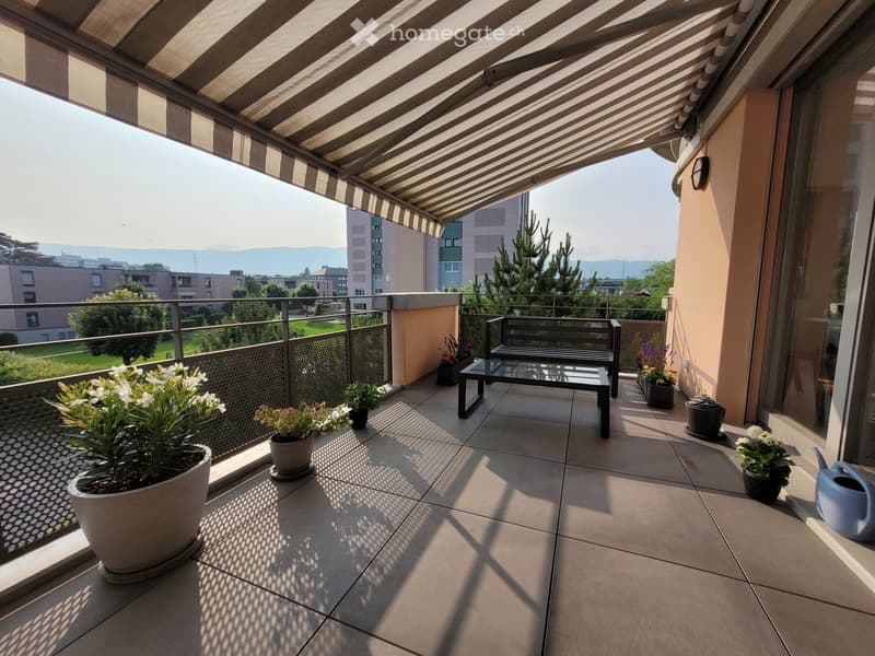 Balcony with a striped awning, tiled floor, bench, small table, and several potted plants.