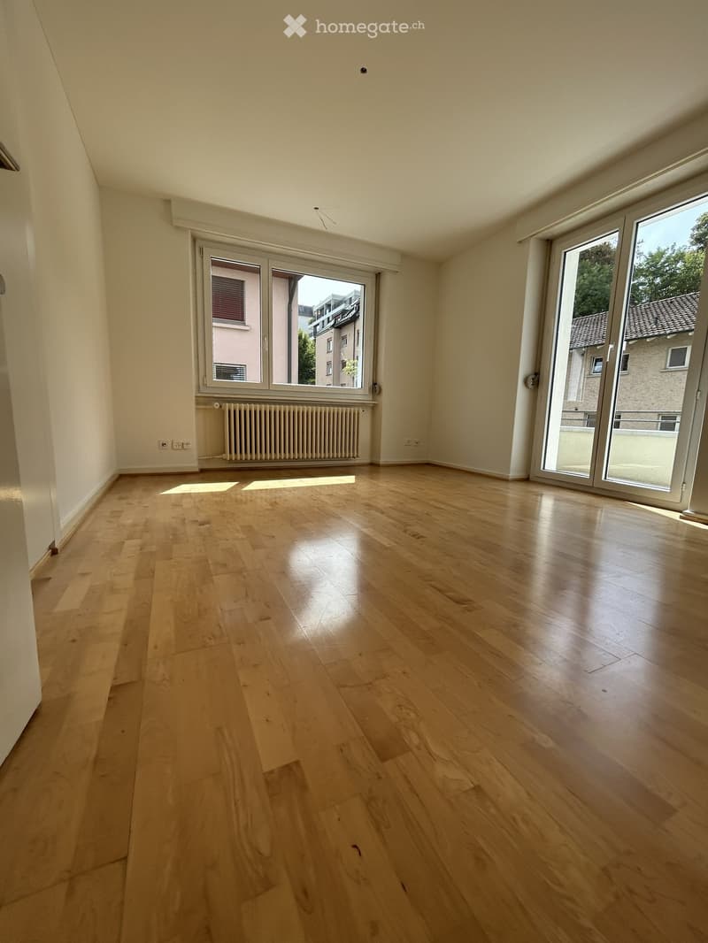 Empty room with light wooden flooring, large windows, and a radiator. No furniture or equipment present.