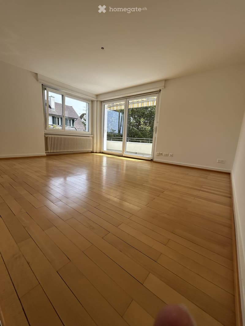 Empty room with wooden flooring, large windows, and sliding glass doors leading to a balcony.