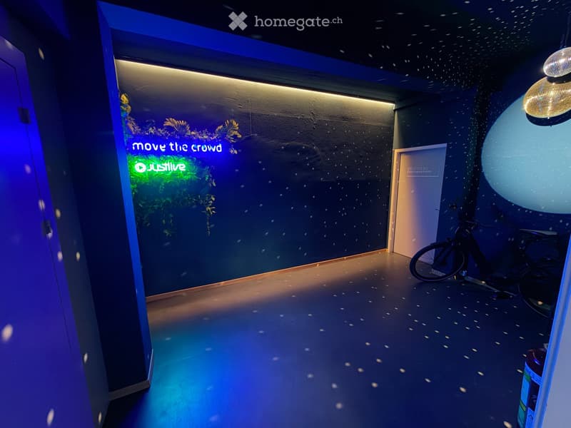 Modern hallway with dark walls, illuminated signage reading "move the crowd" and "JustLive", a bicycle, and a large spherical light fixture.