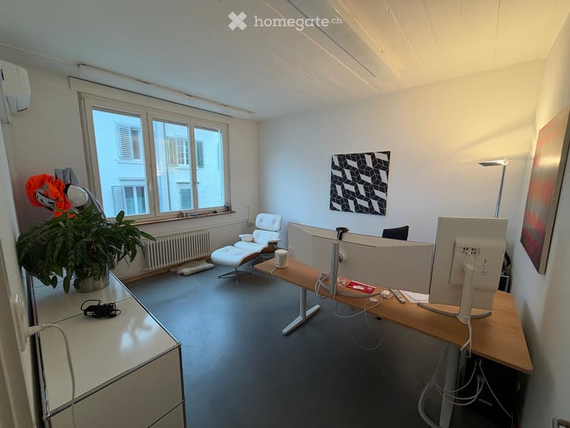 Modern office space with a wooden desk, ergonomic chair, large screen, potted plant, and abstract art on the wall.