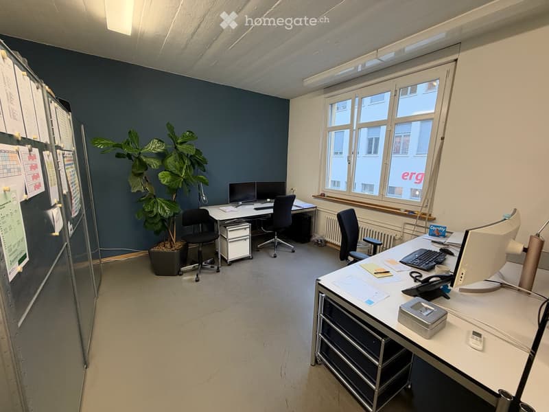 Office space with two desks, chairs, computers, keyboards, a potted plant, and a whiteboard on the wall.