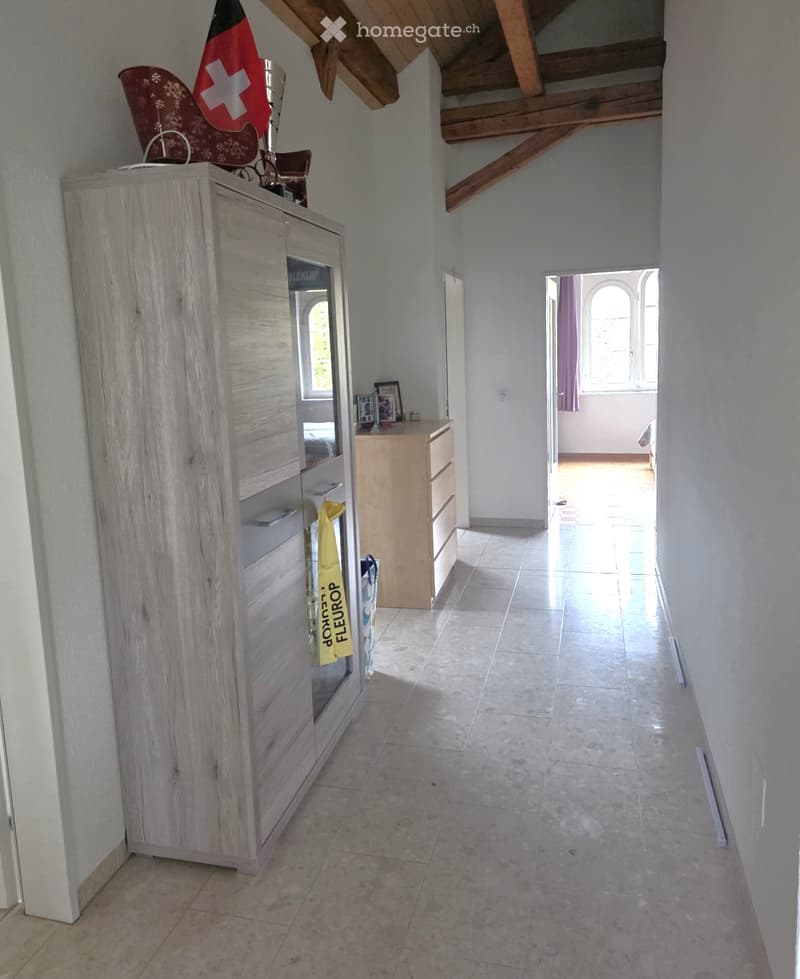 Hallway with tiled floor, wooden wardrobe, small table with items, and visible staircase leading upwards.