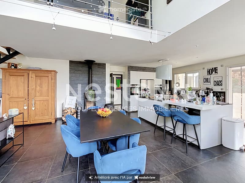 Open-plan living and dining area with a modern kitchen, dining table, and seating. Features include a fireplace, kitchen island with bar stools, and various appliances.