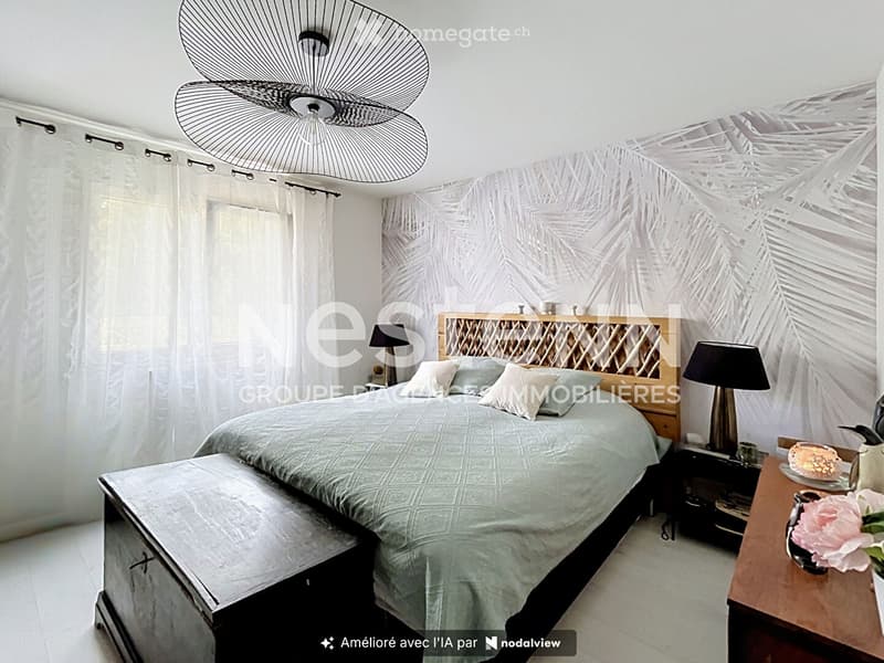 A well-lit bedroom with a large bed, nightstands, a fan, and a decorative flower vase on a wooden table.