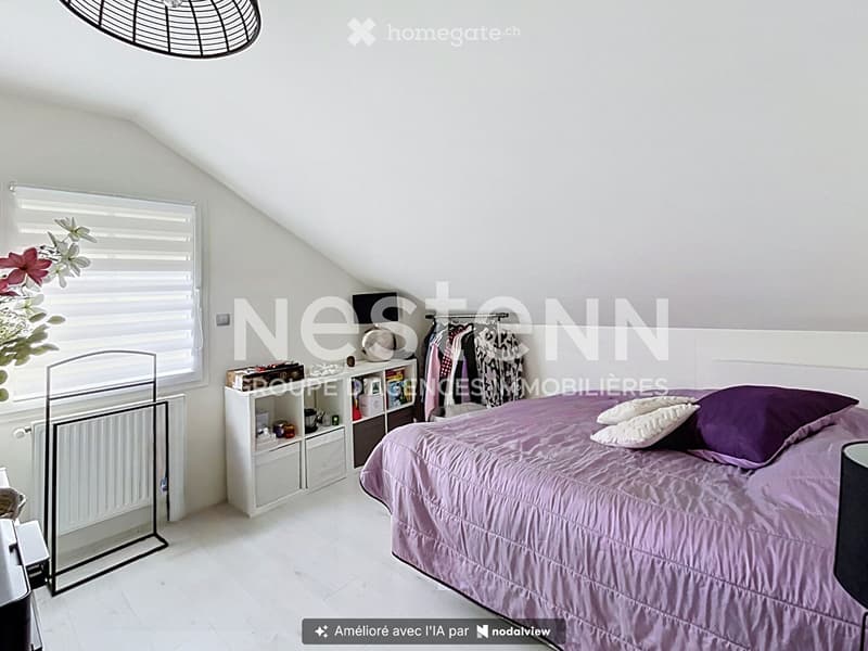 Cozy attic bedroom with a slanted ceiling, white walls, and light wooden flooring. Features a double bed with purple bedding, a nightstand, a radiator, a wardrobe, and a shelf with decorative items.