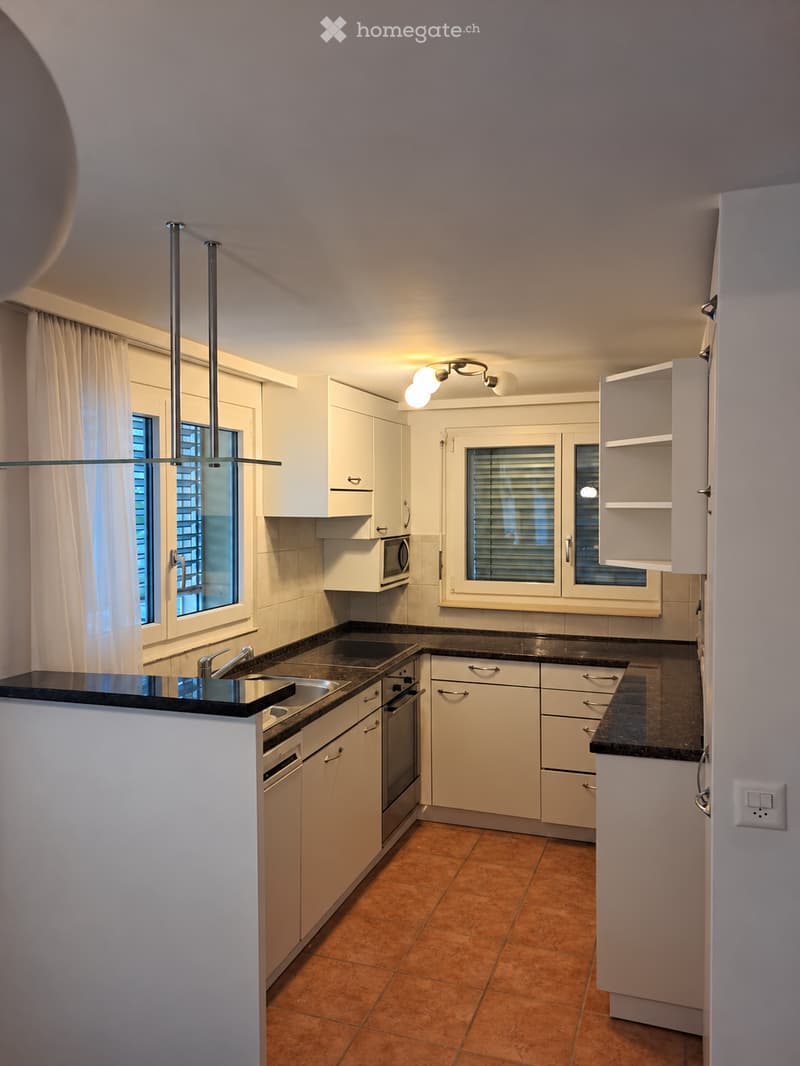 Modern kitchen with white cabinets, black countertops, stainless steel appliances, and a central island with a sink and faucet.