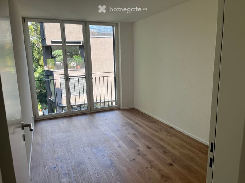 Empty room with light wooden flooring, white walls, and large sliding glass doors leading to a balcony.