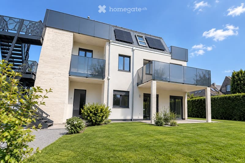 Modern two-story house with white facade, large windows, balconies, solar panels on the roof, and a well-maintained lawn in the front yard.