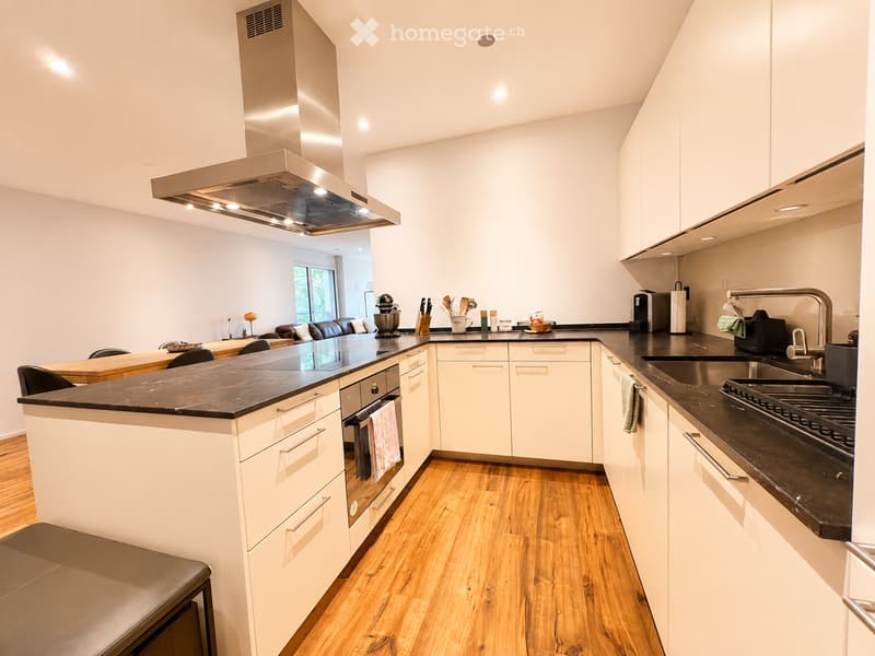 Modern kitchen with white cabinets, black countertops, stainless steel appliances, island with seating, and wooden flooring.