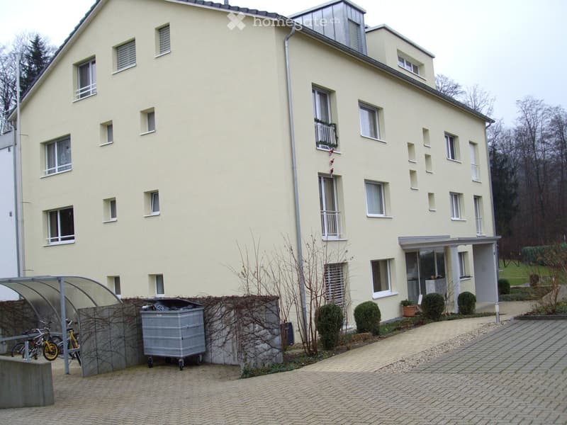 Four-story residential building with light yellow facade, multiple windows, balconies, and a covered entrance area.