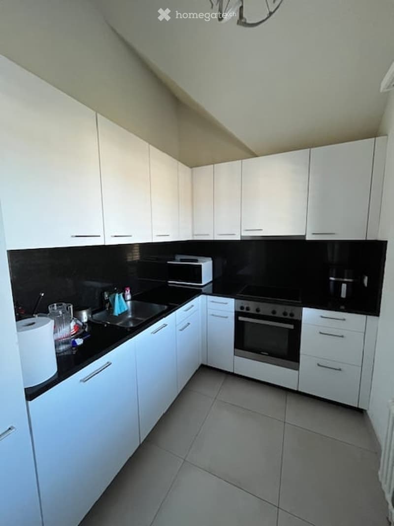 Modern kitchen with white cabinets, black countertops, and stainless steel appliances including a sink, fridge, oven, and microwave. A cup is placed on the counter.
