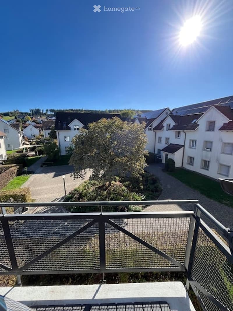 Balcony overlooking a residential area with houses, trees, and a clear blue sky.