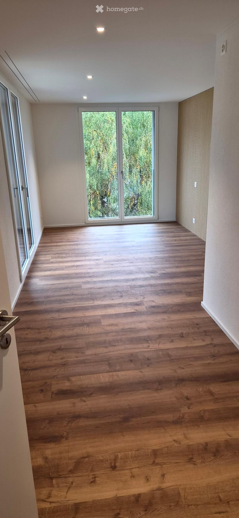Empty room with wooden flooring, large sliding glass doors, and white walls.
