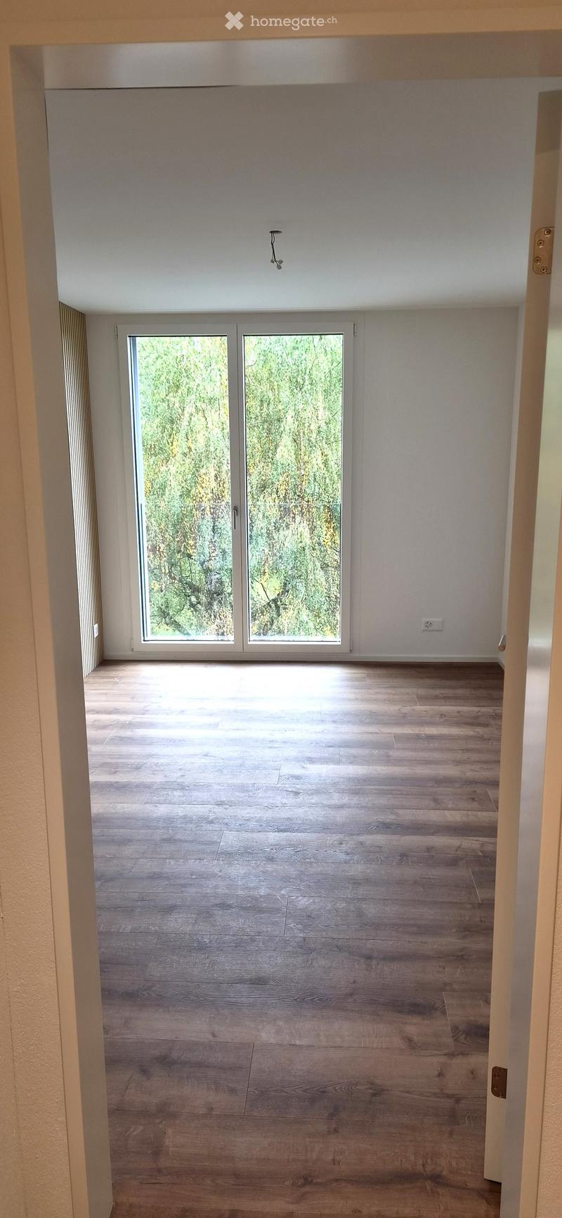 Empty room with wooden flooring, large sliding glass doors leading to an outdoor area, white walls, and a visible electrical outlet.
