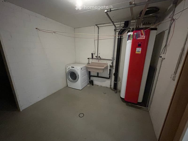 Utility room with a washing machine, sink, and water heater, exposed pipes, and a concrete floor.
