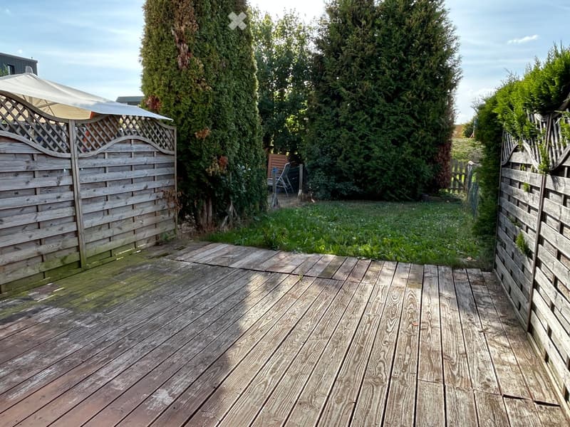 Wooden deck surrounded by tall green trees and wooden fences, with a small canopy and a grassy area beyond.