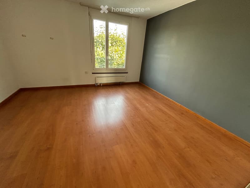 Empty room with wooden flooring, light-colored walls, and a window with a radiator below it.