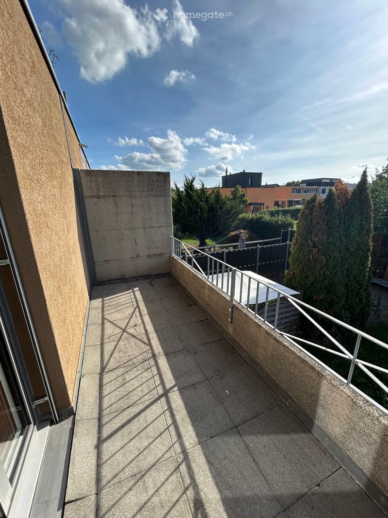 Balcony with tiled floor, metal railing, and view of greenery and neighboring buildings.