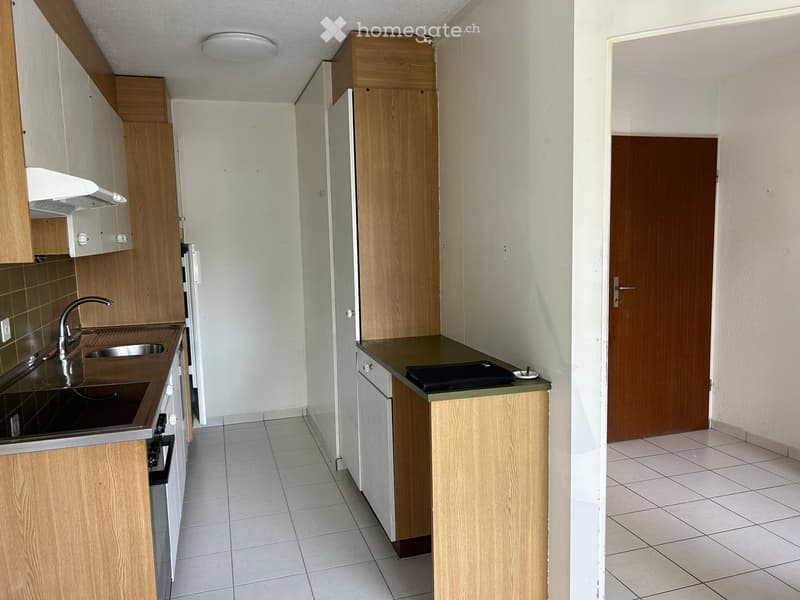 Modern kitchen with wooden cabinets, stainless steel sink, and countertop. The space includes an oven and a small countertop with a black item on it.