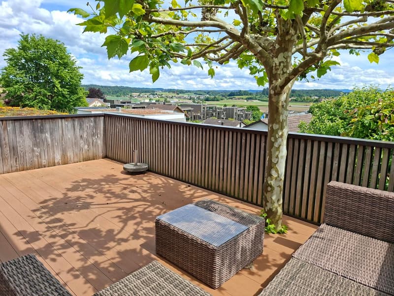 Balcony / Terrace. Wooden deck with wicker furniture, including a sofa, table, and chairs, surrounded by a wooden railing and a tree, with a scenic countryside view.