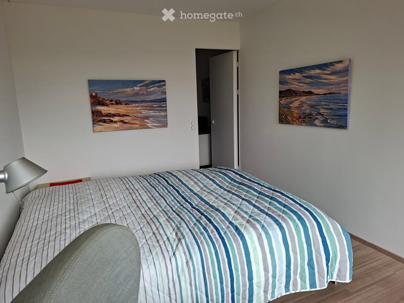 Bedroom. Bedroom with a neatly made bed, striped blue and white bedding, a bedside lamp, and two paintings of coastal scenes on the walls.