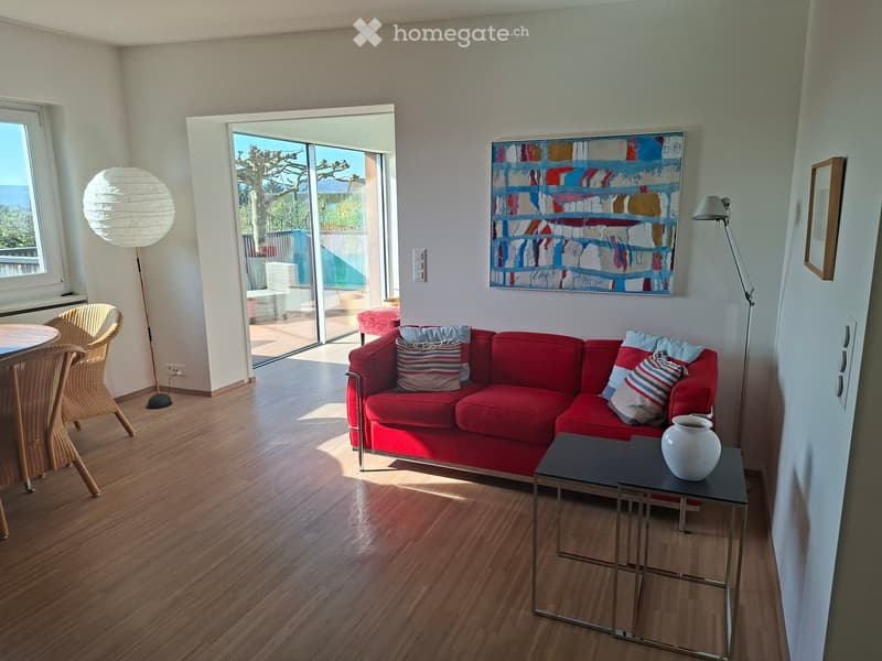 Living Room. Modern living room with wooden flooring, red sofa, coffee table, chairs, and a view through large windows and sliding doors.