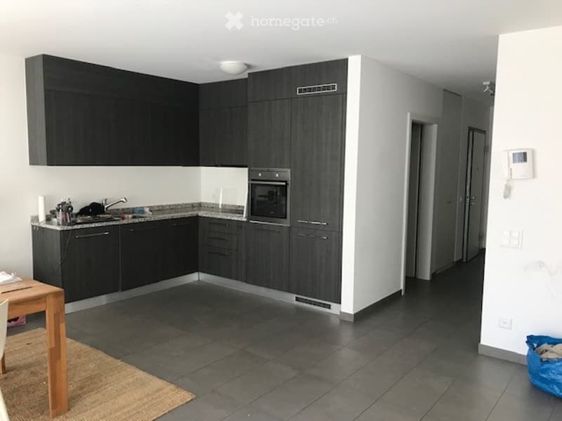 Modern kitchen with dark grey cabinets, stainless steel oven, granite countertop, and a small wooden dining table with chairs.