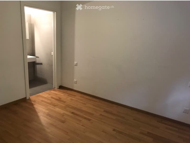 Empty room with wooden flooring and white walls, featuring a doorway leading to another room with a sink visible.