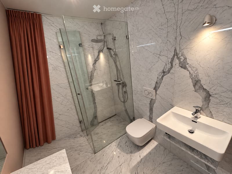 Modern bathroom with marble walls and floor, featuring a glass-enclosed shower, a toilet, a sink with a modern faucet, and a brown curtain.