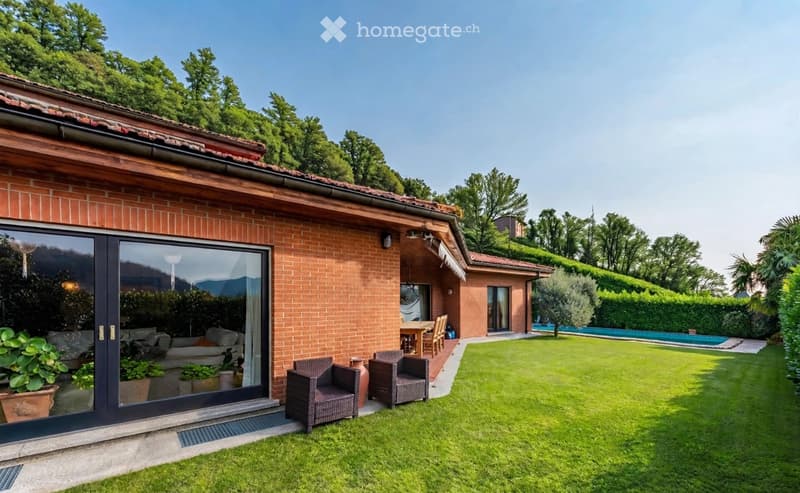 Well-maintained garden with a swimming pool, outdoor seating area, and a view of surrounding greenery and mountains.