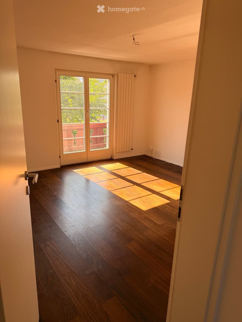 Empty room with wooden flooring, white walls, and a large glass door leading to a balcony or outdoor area.