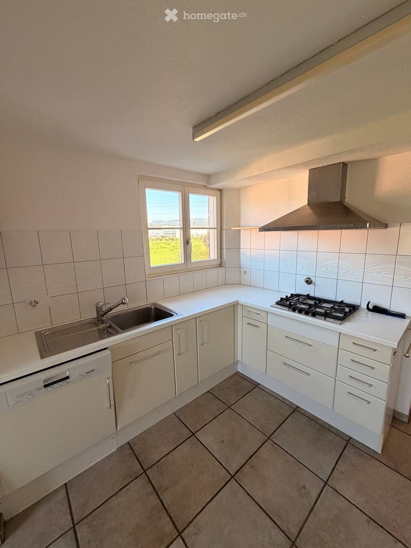Modern kitchen with white cabinets, a gas stove, a sink, and a dishwasher. The room features tiled walls and a tiled floor, with a window offering a view of the outdoors.