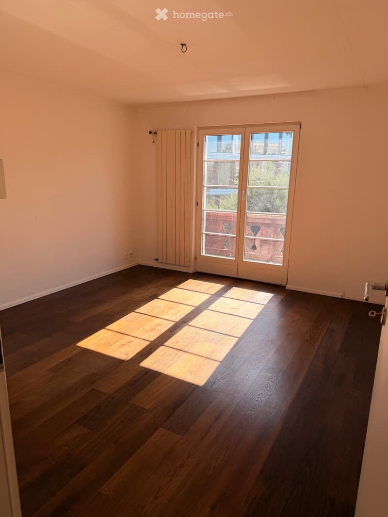 Empty room with wooden flooring, large sliding glass doors leading to a balcony, and a radiator on the wall.