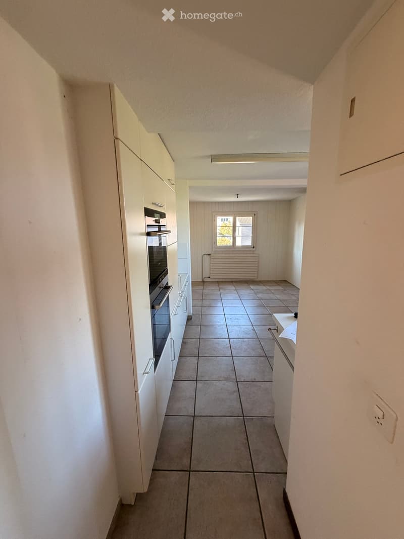 Empty hallway with tiled floor, white walls, and a window at the end. No furniture or items visible.