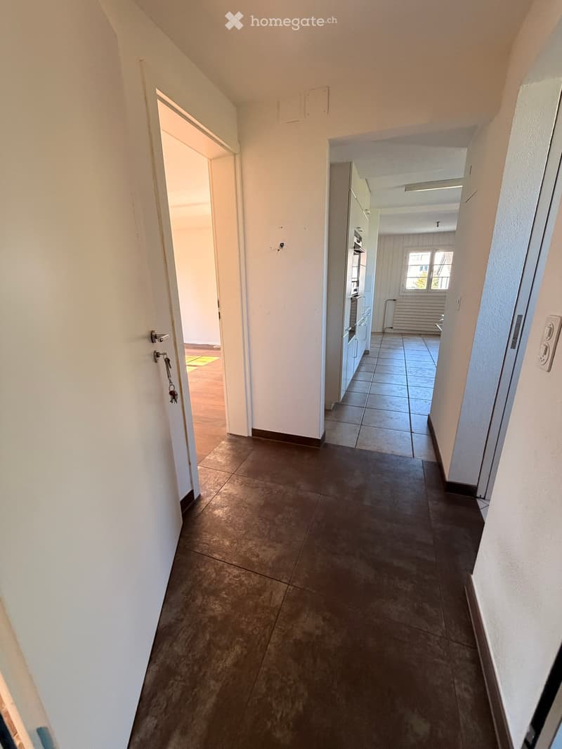 A long, narrow hallway with tiled flooring and white walls, featuring several doors leading to different rooms.