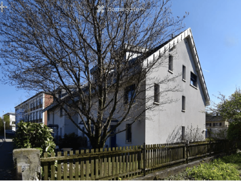 Two-story residential house with white exterior, multiple windows, and a wooden fence in front.