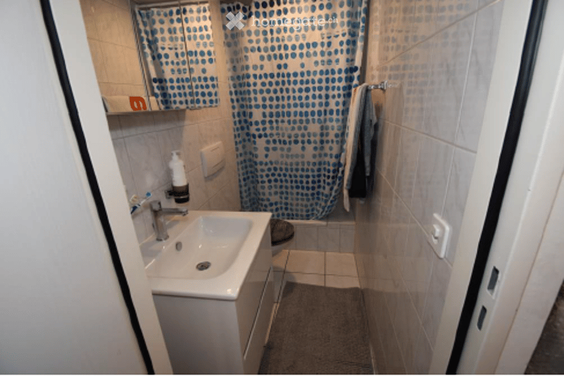 Small bathroom with white tiled walls, a white sink with a chrome faucet, a mirror above it, a blue and white patterned shower curtain, and a towel hanging on a rack.